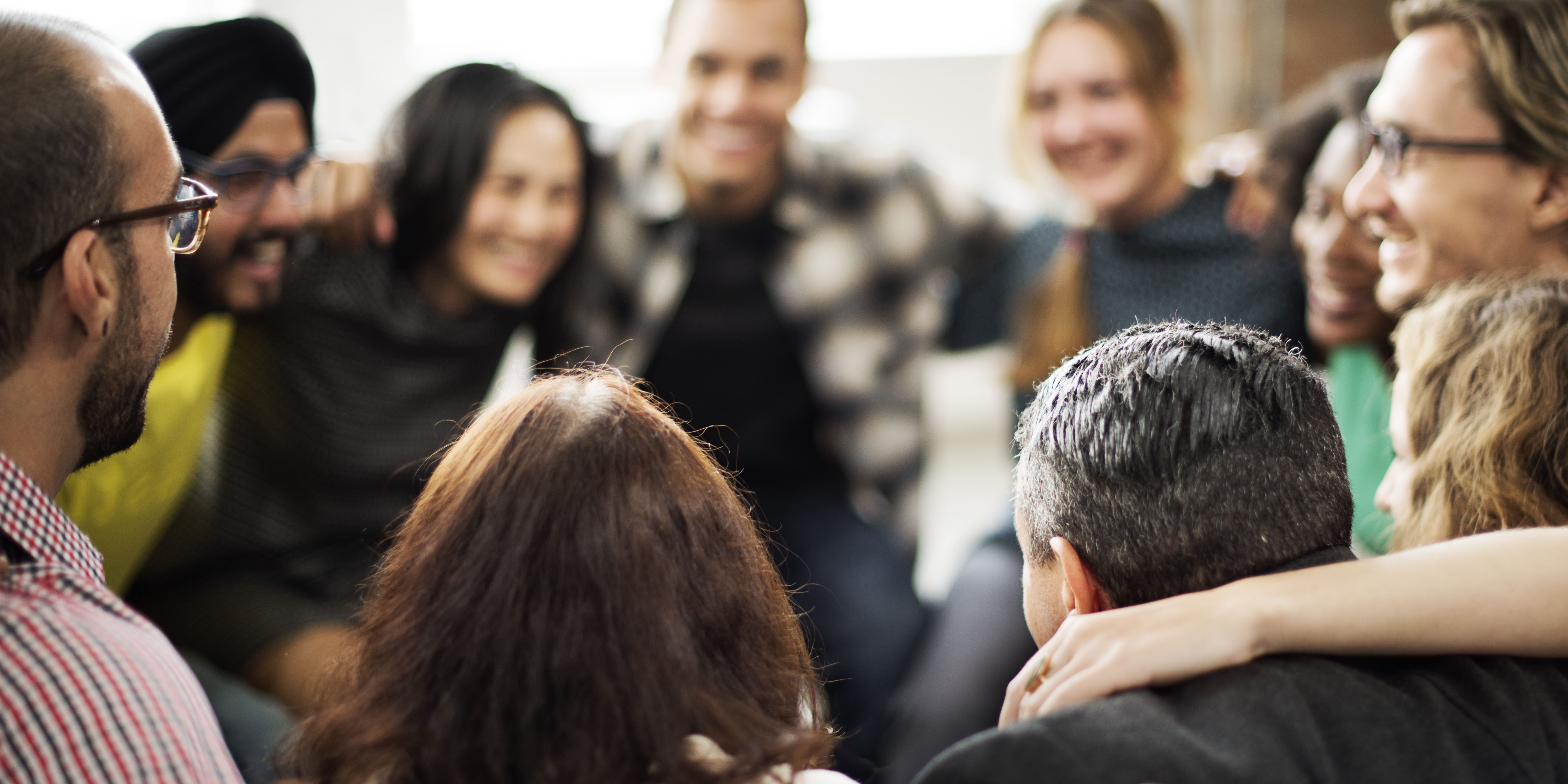 Image of a team of smiling colleagues standing in a circle, some with arms around each others' shoulders