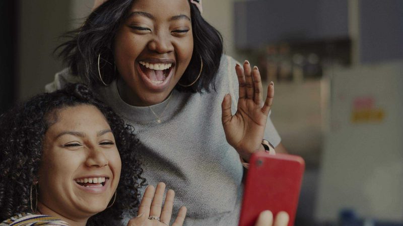 Two people in their late teens or early twenties laughing as they looks into a red phone. The image was selected as it looks like they could be recording a TikTok together.