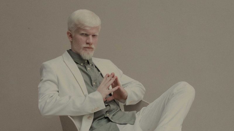 A photo of a man with white hair and beard wearing a white suit looking confidently, if a little arrogantly, down the lens of the camera to us. He is sitting in a designer chair with the ankle of one leg resting on the knee of the other and he's leaning back slightly. This photos is being used to suggest some CEOs may be a little too confident in their ability to be the face of a company.