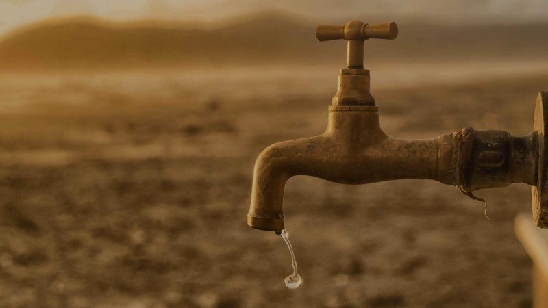 A photo of a brass outdoor tap with a drop of water dripping from its spout. The background is blurred, but is suggestive of a dry, dusty desert. The suggestion here is that a drop of content may be more effective than a larger quantity.