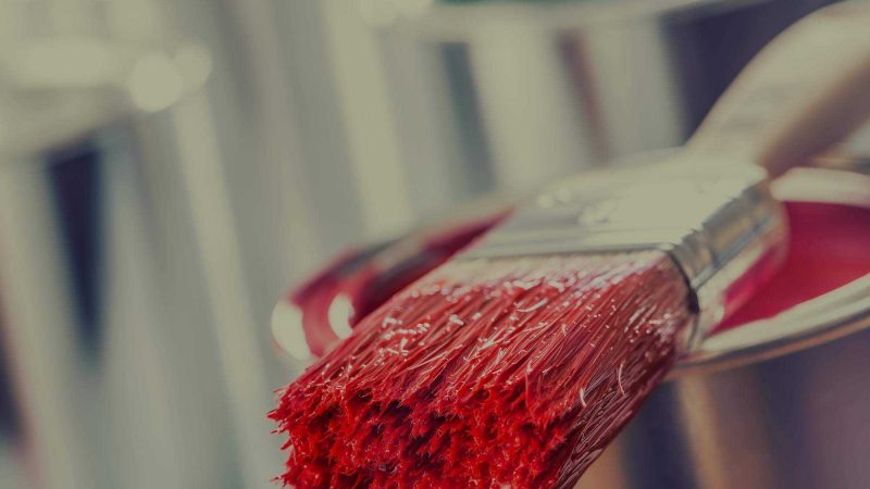 A close up photo of a pain brush which has been dipped in bright red paint and which is resting on the paint pot. This is in reference to article in which the relationship between paint company Dulux and football club Tottenham Hotspur got off to a rocky start.