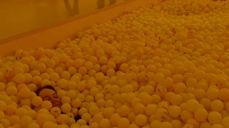An image of a person almost totally submerged in yellow balls in a huge ball pit, suggesting the feeling of being overwhelmed by balls you have to juggle at work.