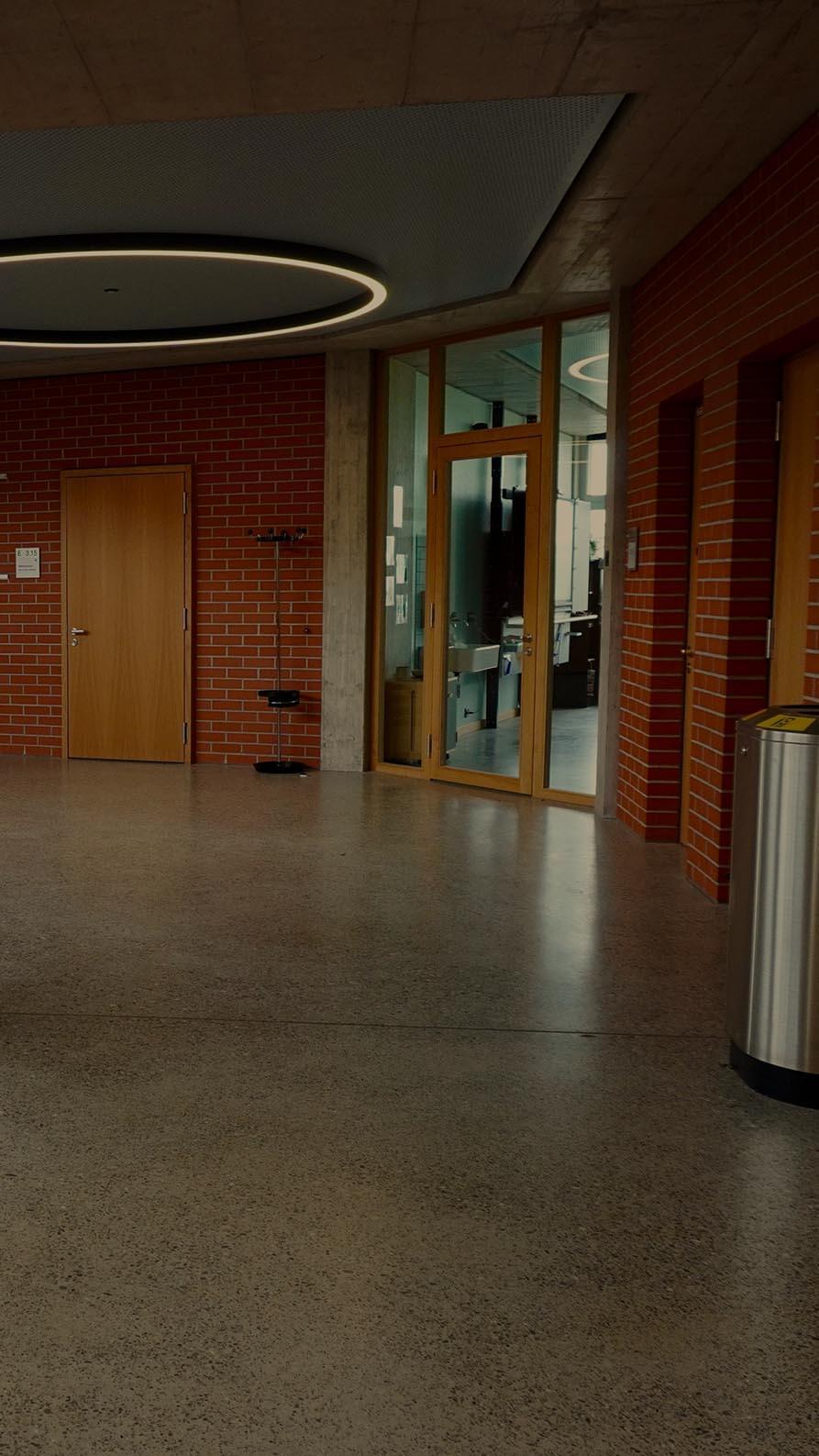 a photo of the interior upper-floor landing of a modern school building. To the left is a staircase rising up to the floor, the walls are redbrick and the colours muted.