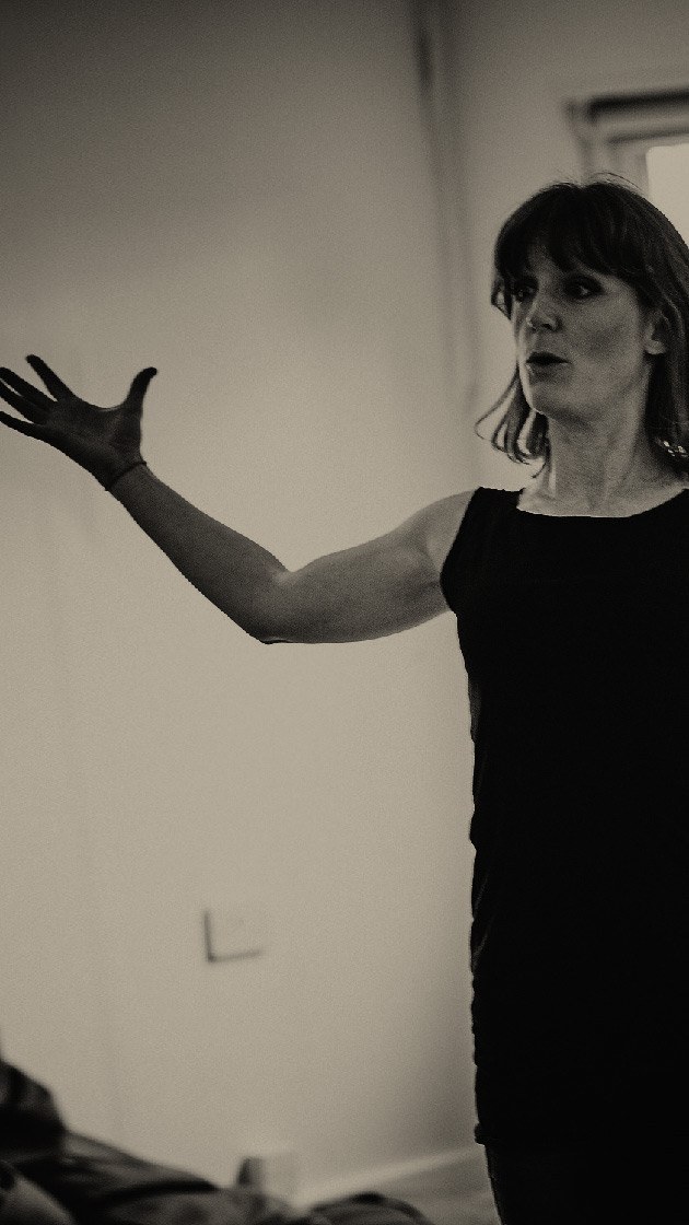 Liz Peters from The Maydays stands with arms stretched wide while presenting to an improvisation group.