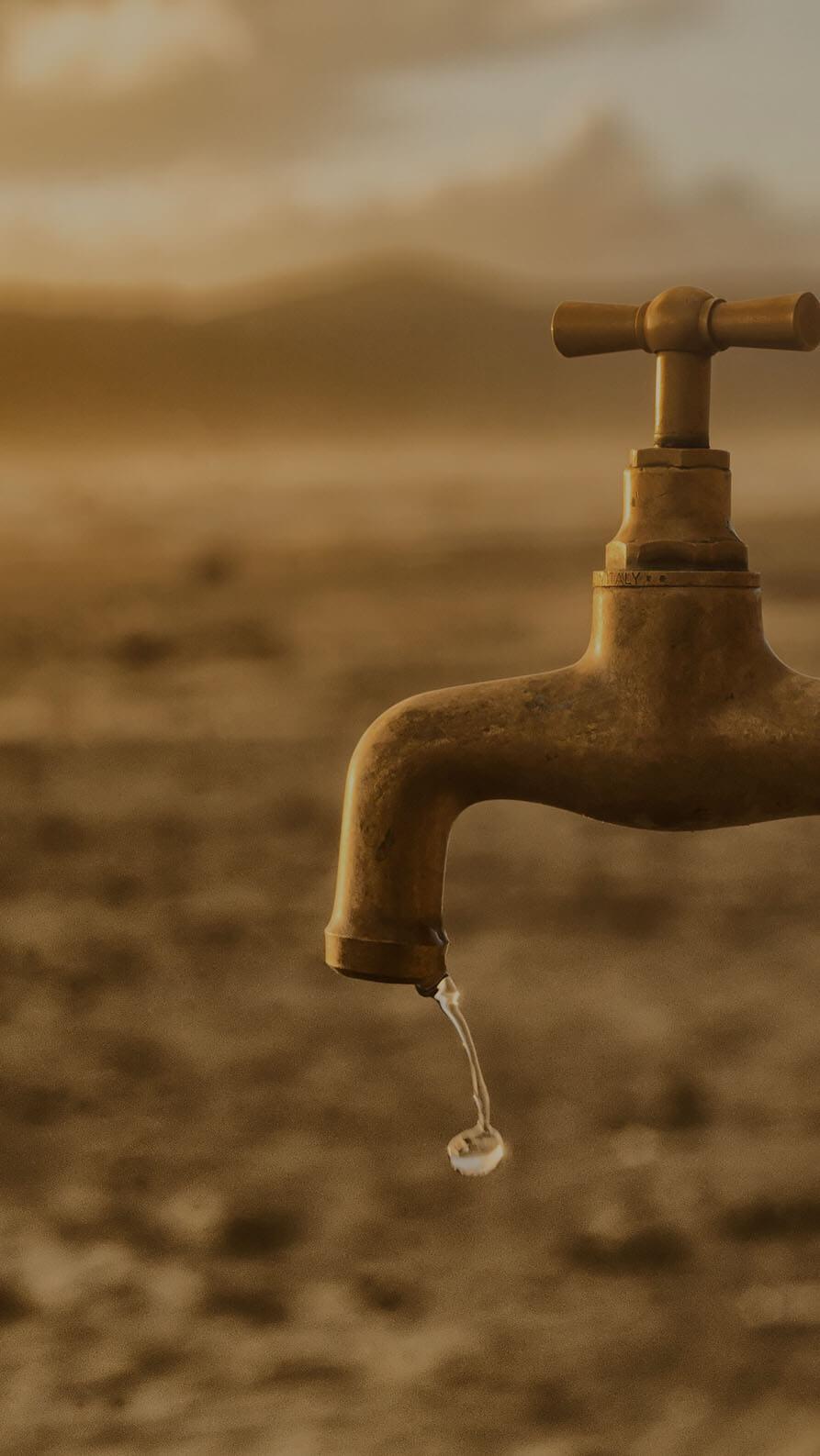 A photo of a brass outdoor tap with a drop of water dripping from its spout. The background is blurred, but is suggestive of a dry, dusty desert. The suggestion here is that a drop of content may be more effective than a larger quantity.